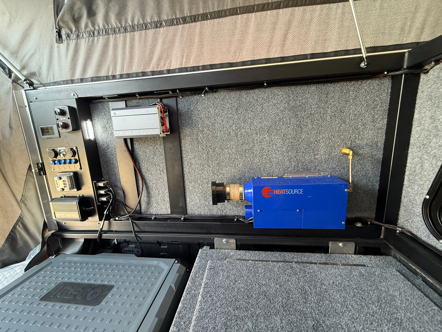 RV rental interior: control panel, Wagan inverter, ICECO fridge, and HEATSOURCE heater for off-grid comfort.