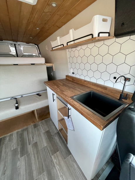 RV rental with a modern interior: compact kitchen, wood counters, hexagonal backsplash, black sink, and versatile bench seating.