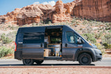 Pet-friendly rv rental van: a gray camper with its side door open, revealing two dogs & custom interior, parked near red rocks.