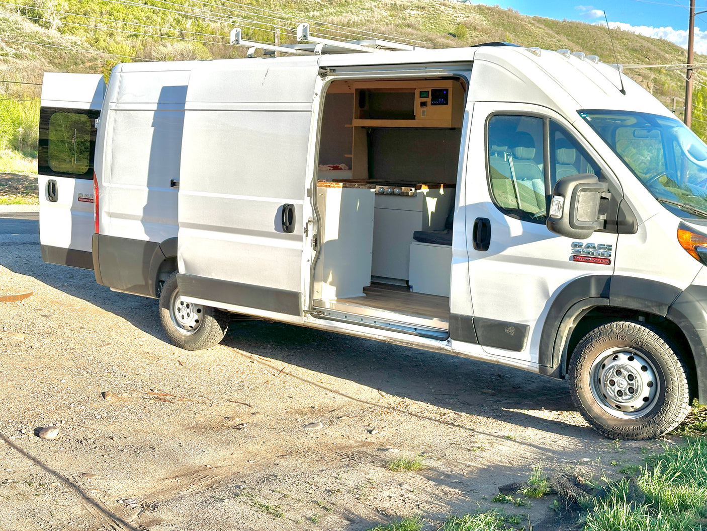 White Ram ProMaster camper van conversion, side door open to show kitchenette and interior setup.