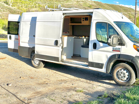 White Ram ProMaster camper van conversion, side door open to show kitchenette and interior setup.
