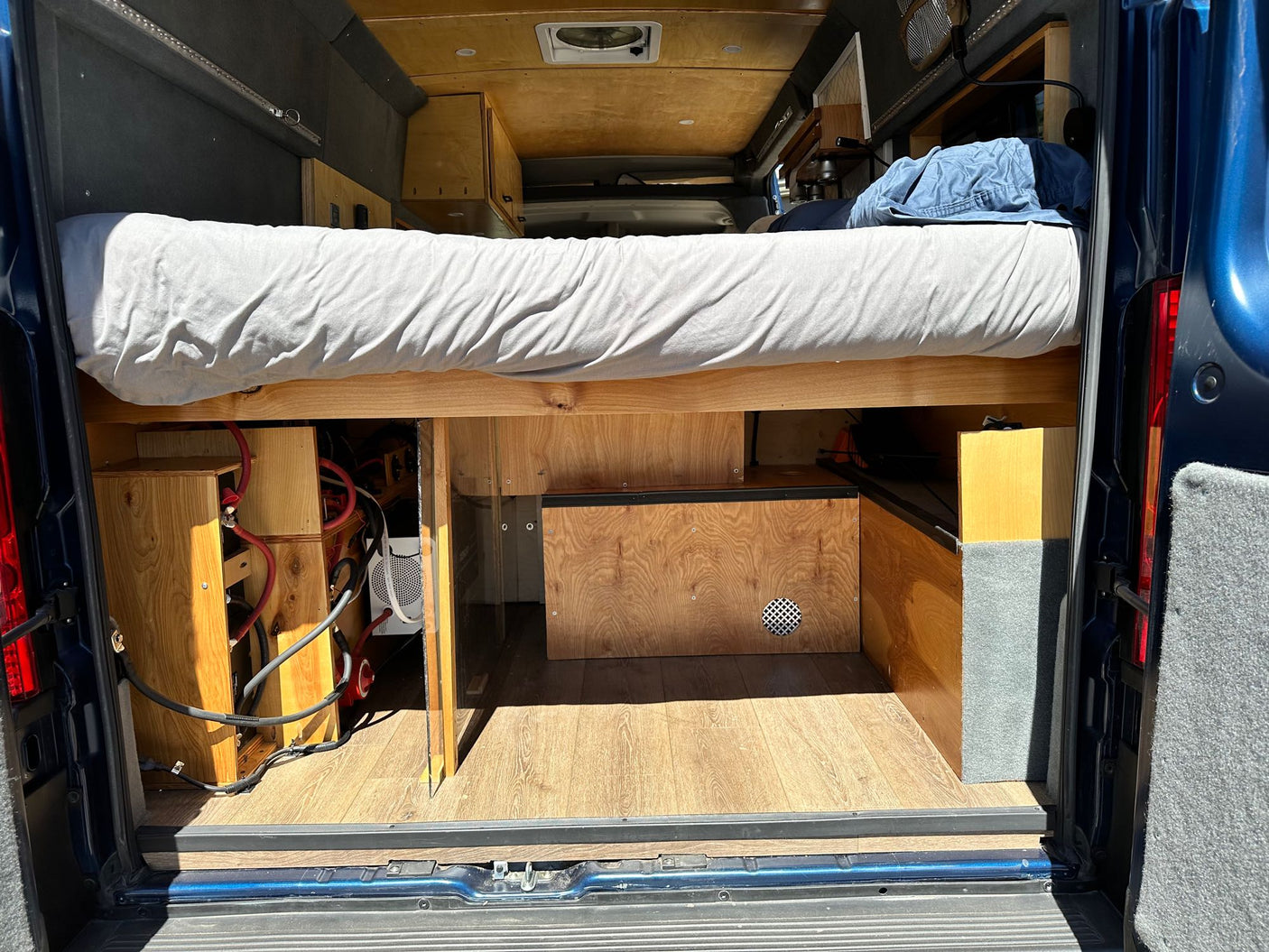 View a custom RV rental interior: raised bed, under-bed storage, and visible electrical components.