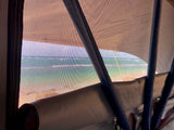 Ocean view from an RV rental through the mesh screen, showing a sandy beach and blue-green water.
