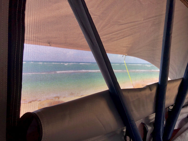 Ocean view from an RV rental through the mesh screen, showing a sandy beach and blue-green water. — photo 6