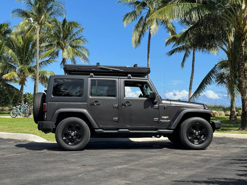 This dark grey Jeep Wrangler, equipped with a rooftop tent for RV rental adventures, is parked under palm trees on a sunny day. — photo 7