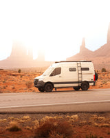 White RV rental on a desert road at sunrise, surrounded by iconic red rock formations. Ideal for unforgettable adventures.