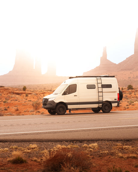 White RV rental on a desert road at sunrise, surrounded by iconic red rock formations. Ideal for unforgettable adventures.