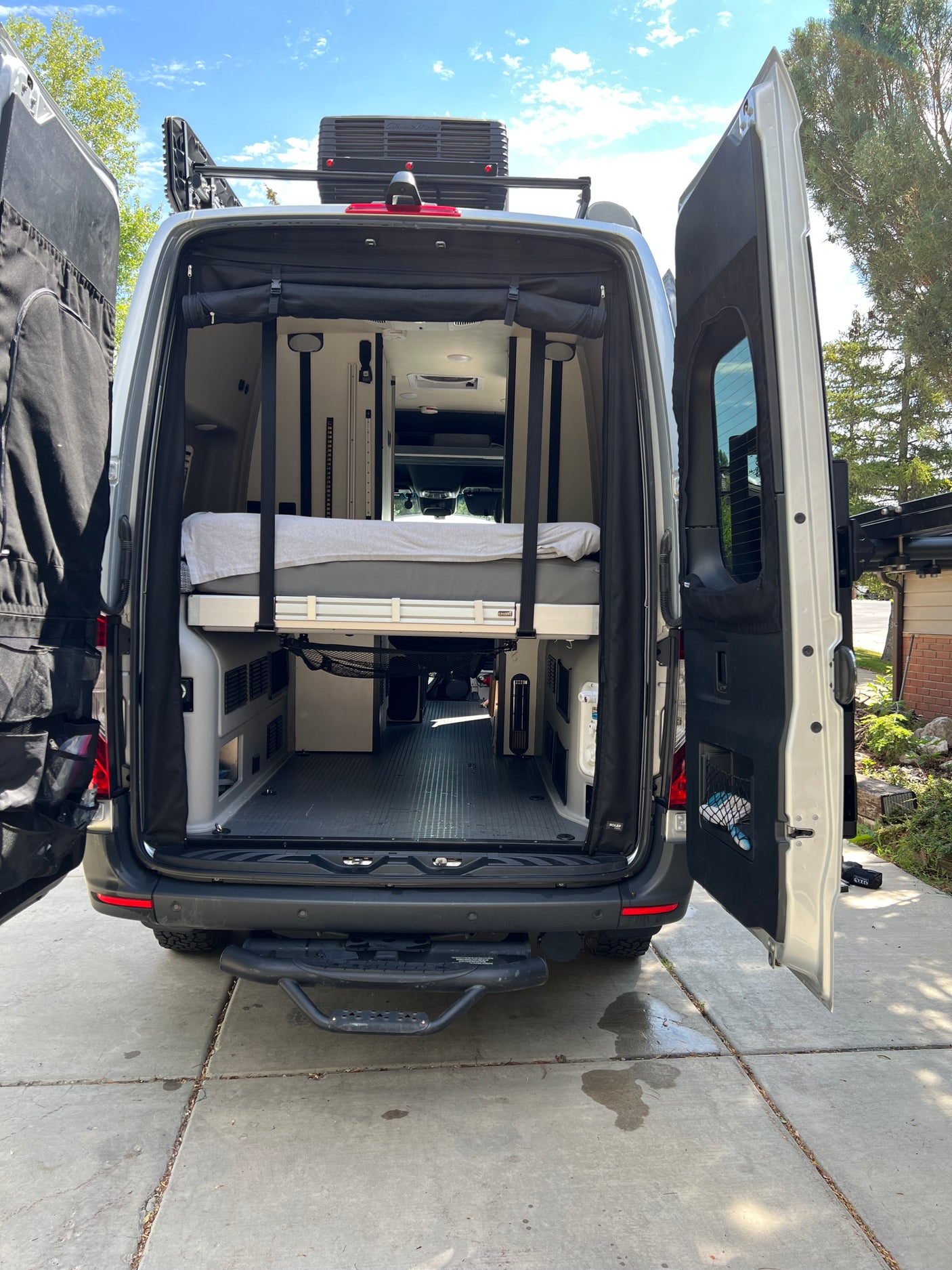 Open rear doors of an RV rental show a spacious interior with an elevated bed & storage for adventures.