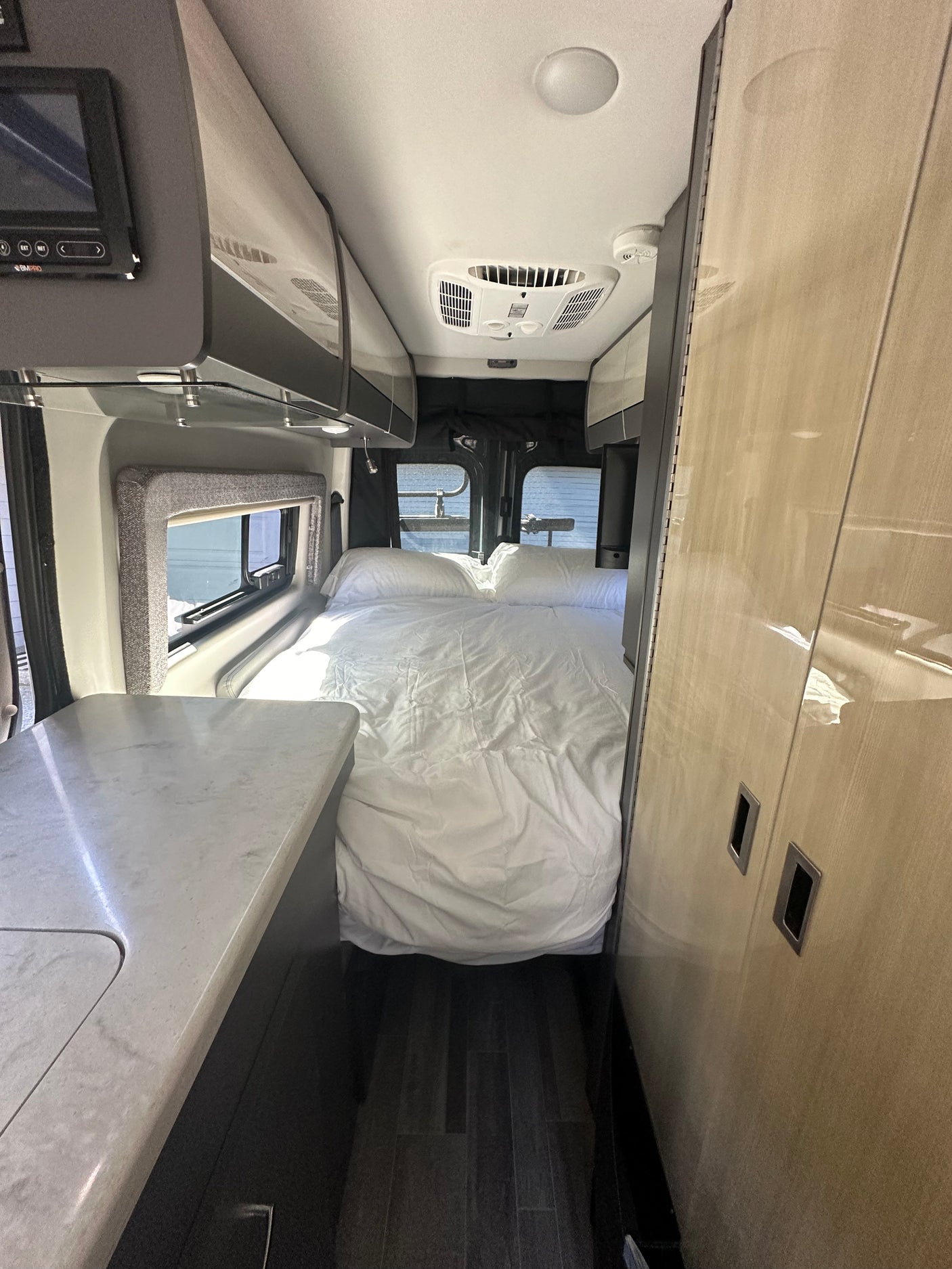 Comfortable rv rental interior: full bed, modern kitchen counter, and overhead storage, perfect for adventures.