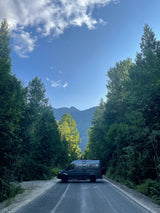 Scenic rv rental parked on a forest road, with majestic mountains in the distance under a blue sky.