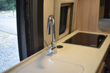 Compact RV rental kitchen with modern chrome faucet, integrated sink, and cooktop, overlooking an outdoor road.