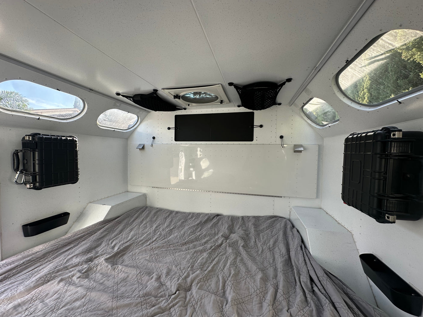 Explore this RV rental's interior: bed, porthole windows, ceiling fan, and secure wall-mounted storage cases.