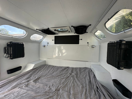 Explore this RV rental's interior: bed, porthole windows, ceiling fan, and secure wall-mounted storage cases.