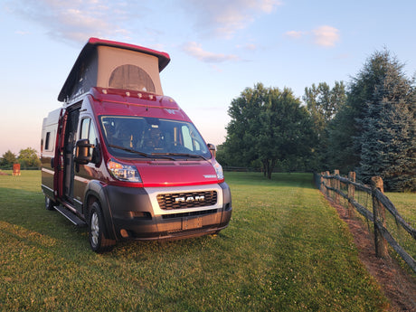 Red Winnebago camper van RV rental, pop-top open, ready for adventure on a grassy field at golden hour.