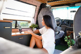 An Asian woman works on her laptop in a bright, modern RV rental. Enjoying mobile remote work and the van life lifestyle.
