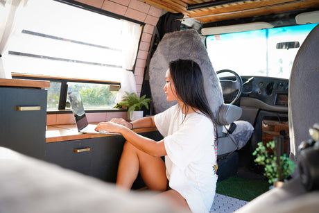 An Asian woman works on her laptop in a bright, modern RV rental. Enjoying mobile remote work and the van life lifestyle.