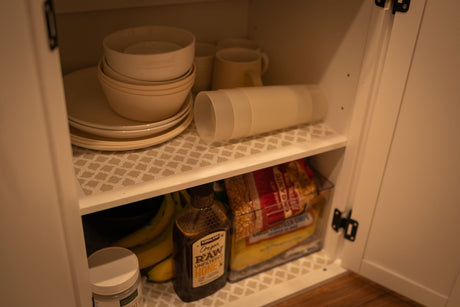 Organized RV rental storage: cabinet with plates, bowls, cups, honey, bananas, and snacks on patterned shelf liners.