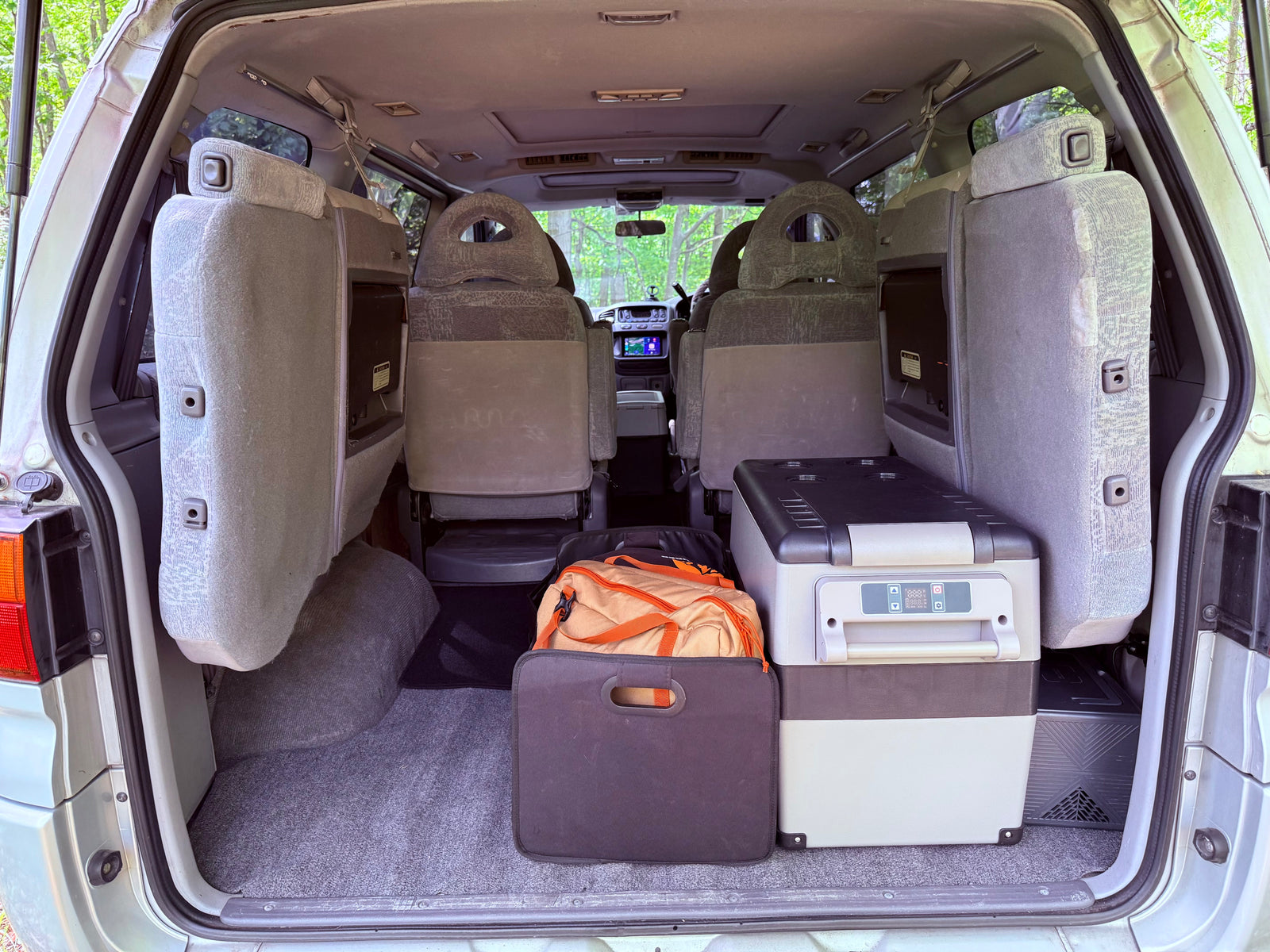 RV rental van's cargo area: Portable fridge, bags, and rearranged seats, ready for a camping trip.
