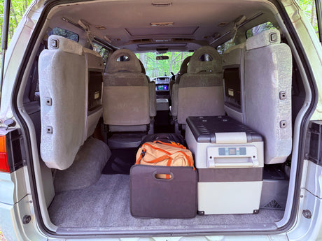 RV rental van's cargo area: Portable fridge, bags, and rearranged seats, ready for a camping trip.