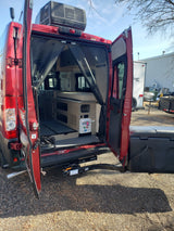 Red RV rental camper van with open back doors, showing interior living space, roof AC, and rear hitch/cargo box. Ready for adventure.