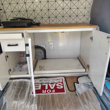 RV rental interior: a neat camper kitchen with white cabinets, pull-out storage, an electrical outlet, and stylish geometric tile.