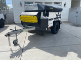 This black & white overland camper trailer with yellow recovery boards is ideal for RV rental adventures.