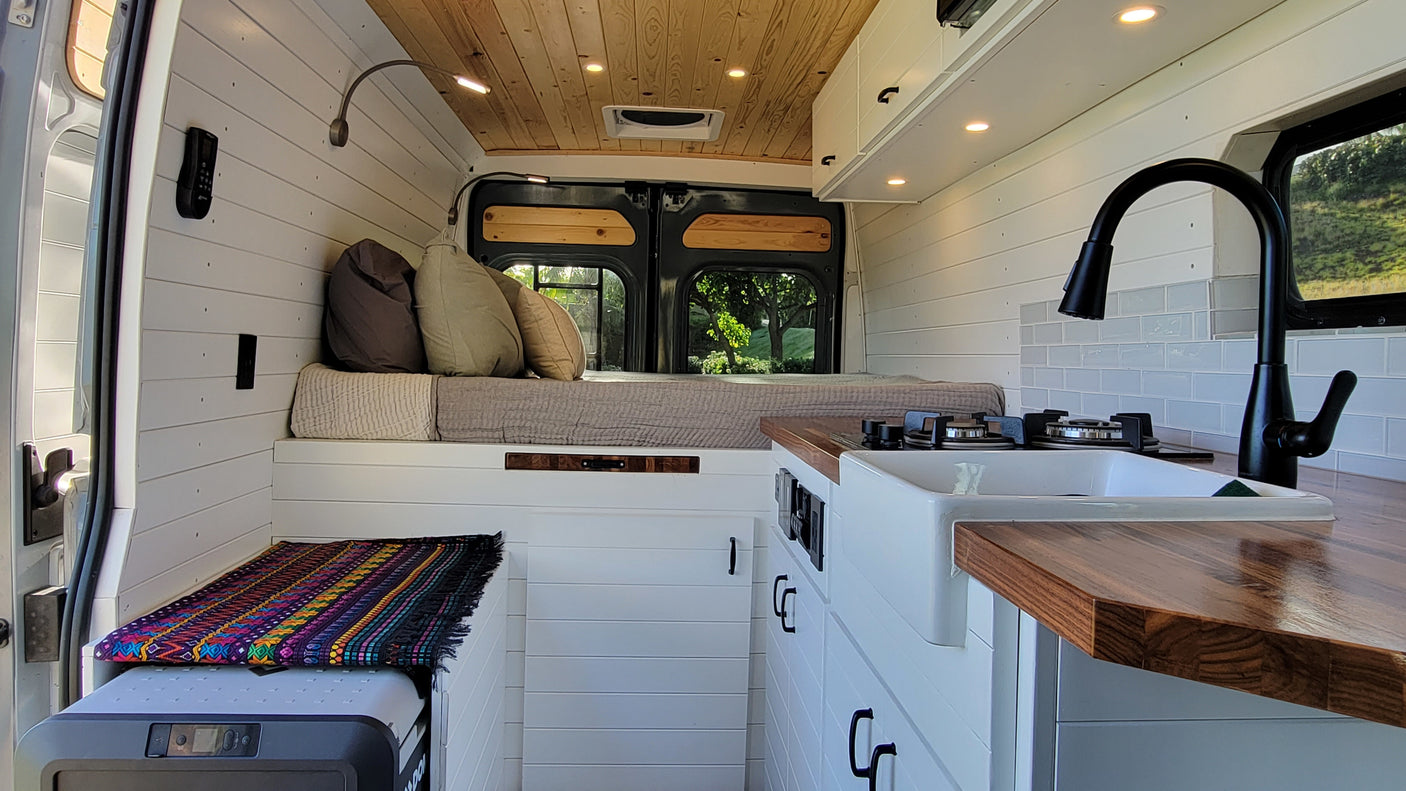 Experience comfort in this stylish RV rental's interior, featuring a cozy bed, modern kitchenette, and warm wood accents.