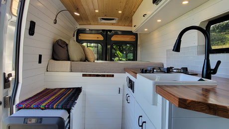 Experience comfort in this stylish RV rental's interior, featuring a cozy bed, modern kitchenette, and warm wood accents.