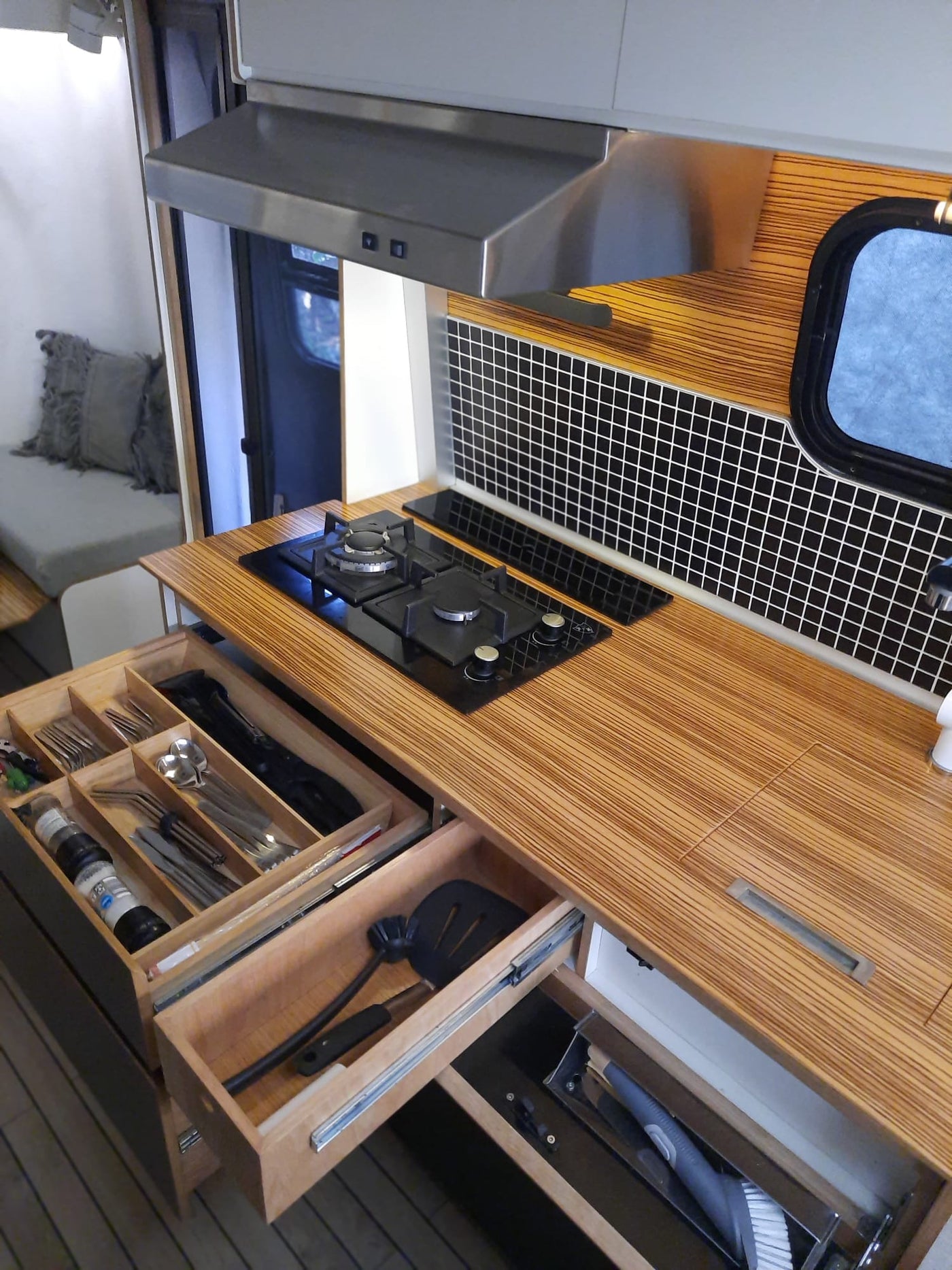 Smart RV rental kitchen with a gas stove, range hood, and open drawers revealing organized cutlery and cleaning supplies. — photo 10