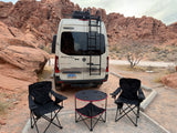 Enjoying a desert campsite with a Winnebago RV rental. Camper van, chairs, and table surrounded by red rock formations.