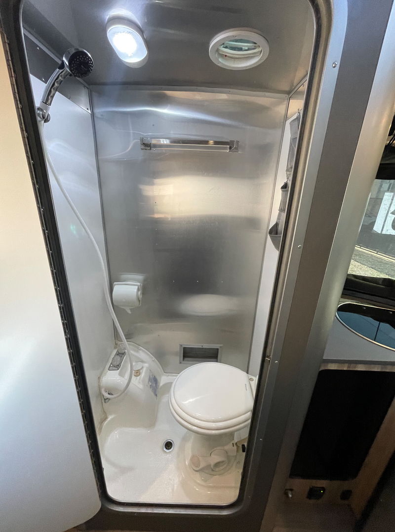 Inside an rv rental, a shiny, compact wet bath featuring a toilet, handheld shower, and bright overhead light. — photo 6