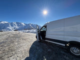 White van on snowy ground, majestic snow-covered mountains under a bright sun. Perfect for your next RV rental adventure!