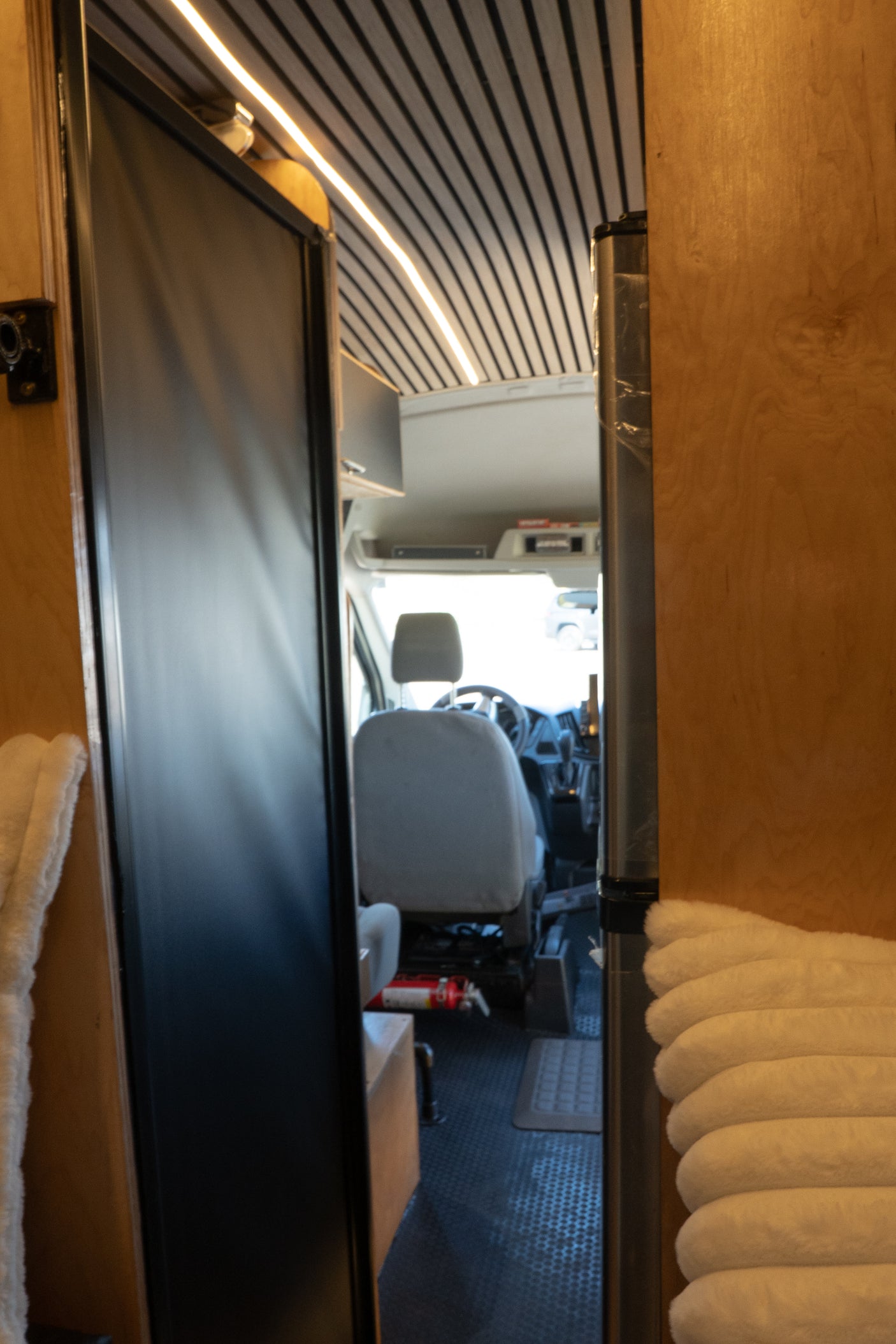 Interior of an RV rental looking toward the front cabin. Shows driver's seat, dashboard, lighting, & safety fire extinguisher.