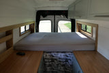 RV rental: Cozy camper van interior with a comfortable bed, wooden accents, storage, and natural light from rear windows.