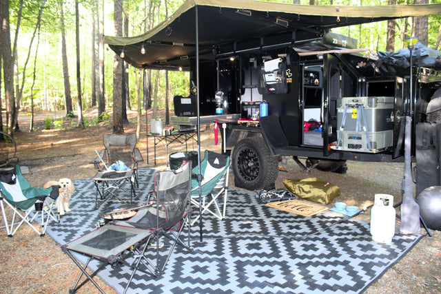 Ultimate outdoor living with this modern overland RV rental setup: kitchen, comfortable chairs, and a happy dog at a serene campsite.