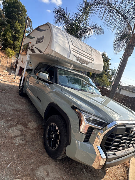 Light green Toyota Tundra truck with a Lance truck camper for rv rental, parked outdoors under palm trees.