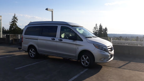 A sleek silver Mercedes-Benz Metris campervan, ideal for RV rental, parked on a sunlit rooftop with distant trees.