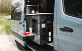 This RV rental features a camper van's open side door revealing a compact outdoor kitchen with a sink and pull-out table.
