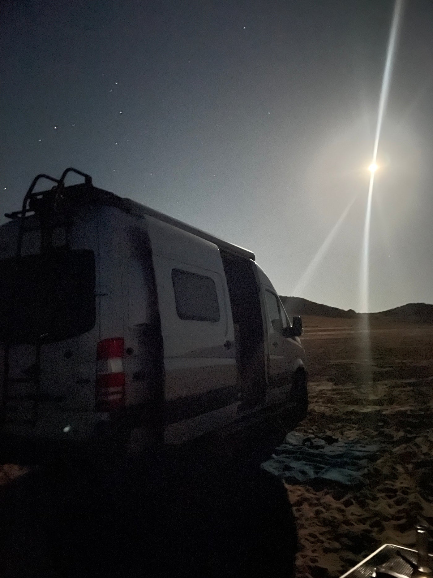 Moonlit RV rental adventure: A white camper van under a starry sky with a bright moon, parked in a remote, sandy landscape. — photo 20
