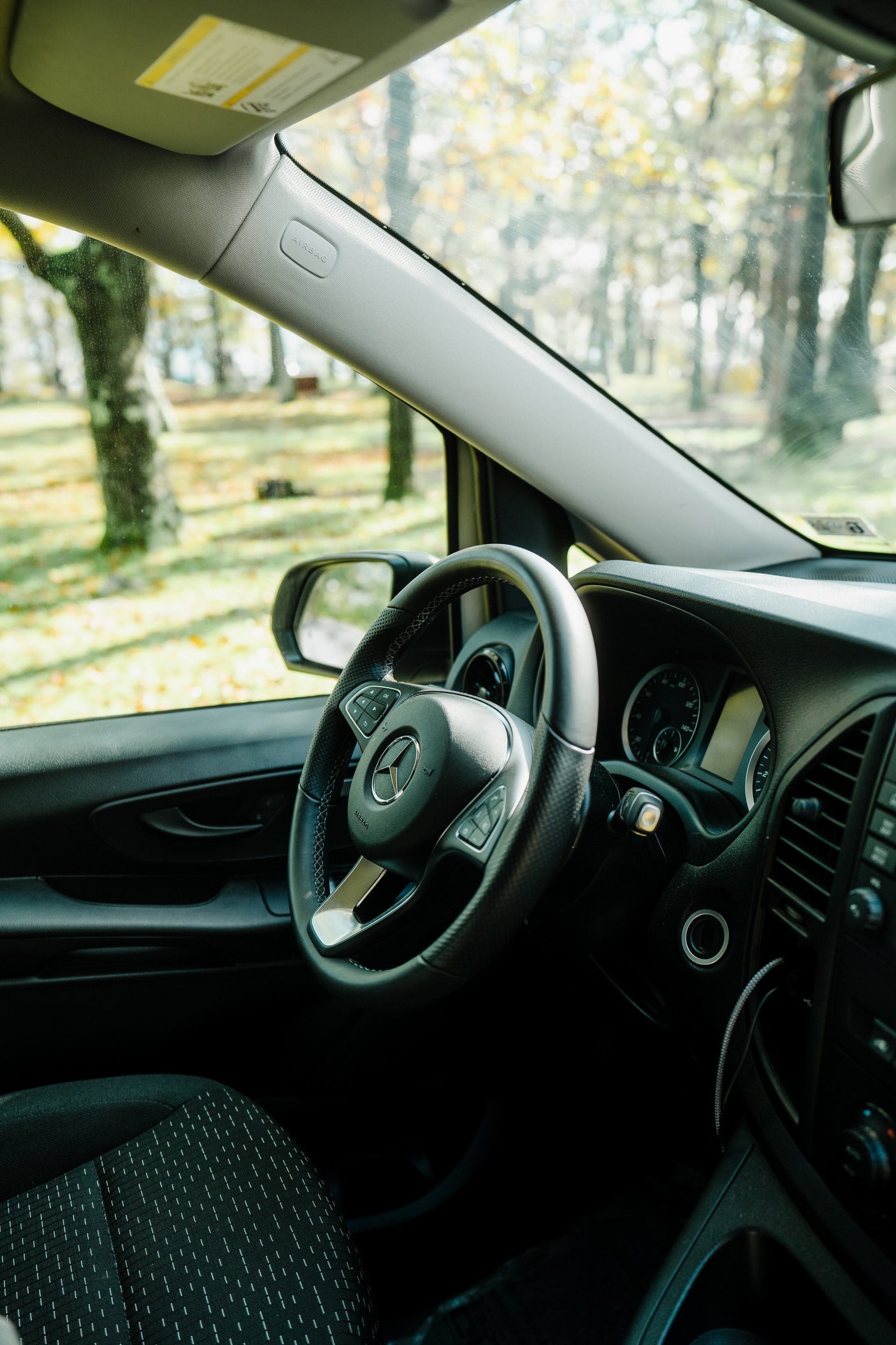 Driver's seat of a modern Mercedes-Benz van, perfect for an RV rental. Features dashboard, steering wheel, and trees outside.