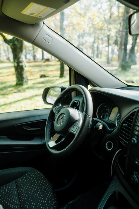 Driver's seat of a modern Mercedes-Benz van, perfect for an RV rental. Features dashboard, steering wheel, and trees outside.