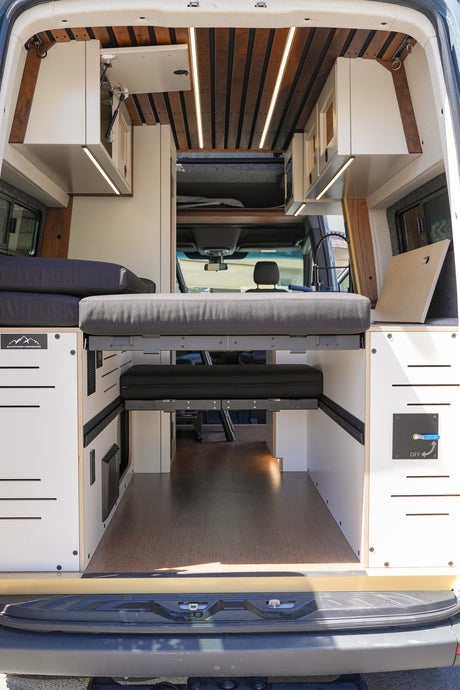 Step into this custom RV rental, featuring a versatile modular bed, overhead storage, and warm ambient lighting.