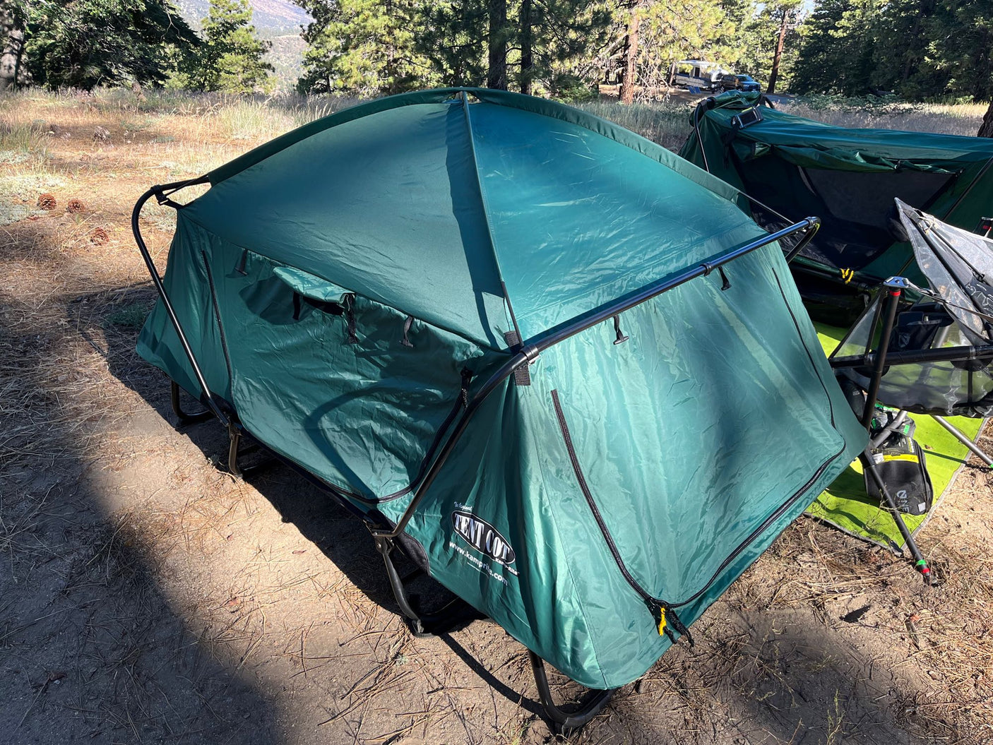 Enjoying camping: a green Tent Cot stands ready at a sunny site, with an RV rental in the distance.