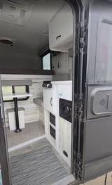 Cozy rv rental interior featuring a bunk bed, compact kitchenette, and dining booth with rustic wood-paneled walls.