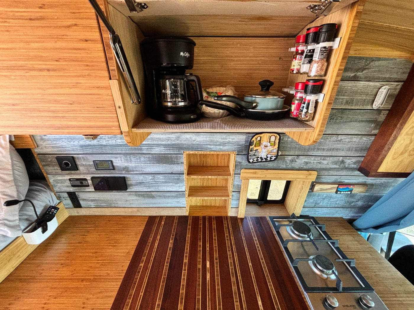 Inside an RV rental, a functional kitchen with a coffee maker, Gasland cooktop, spices, and beautiful wood finishes. — photo 12