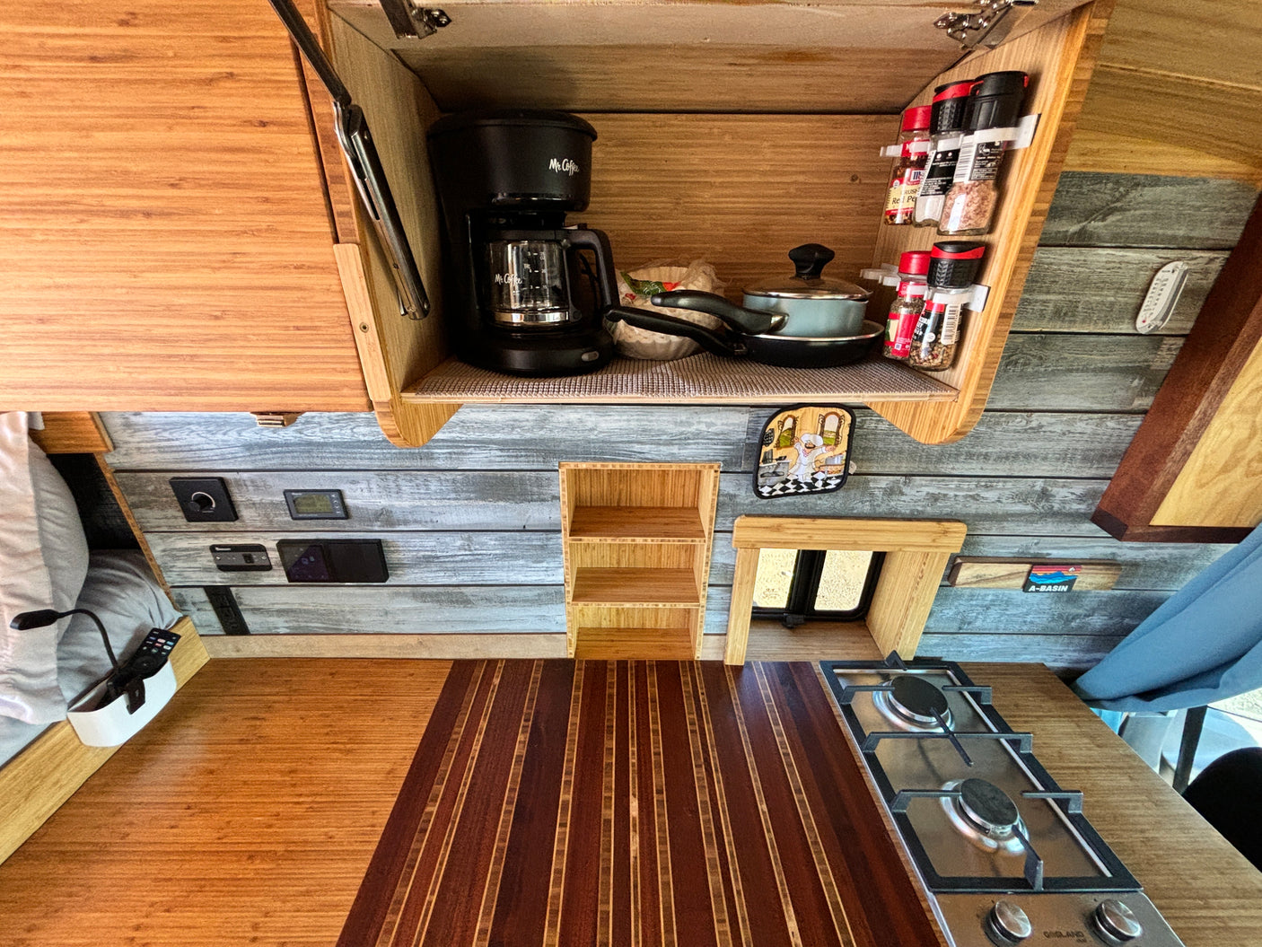 Inside an RV rental, a functional kitchen with a coffee maker, Gasland cooktop, spices, and beautiful wood finishes.
