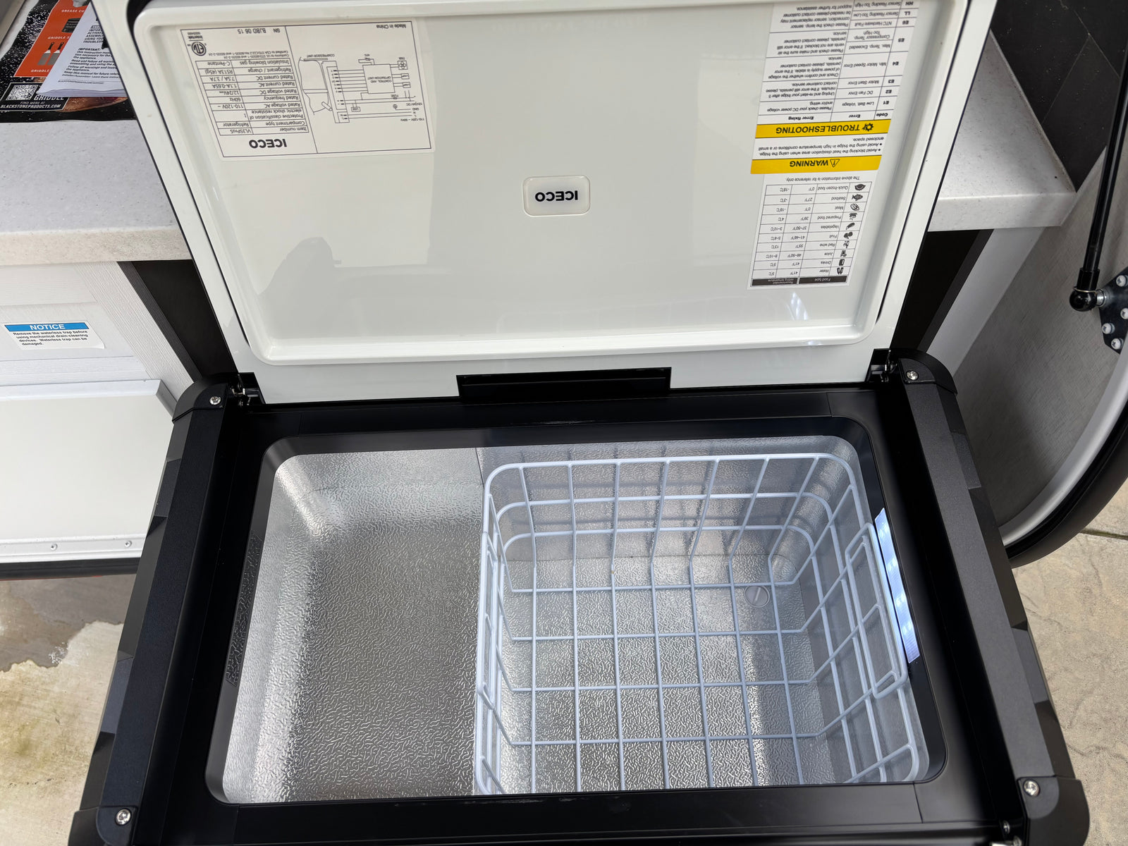 Open ICECO portable fridge/freezer for your rv rental. Interior shows a wire basket and product info on the lid.