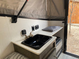 RV rental interior: compact kitchen with sink, faucet, thermostat, outlets, and charging center in a pop-up camper.