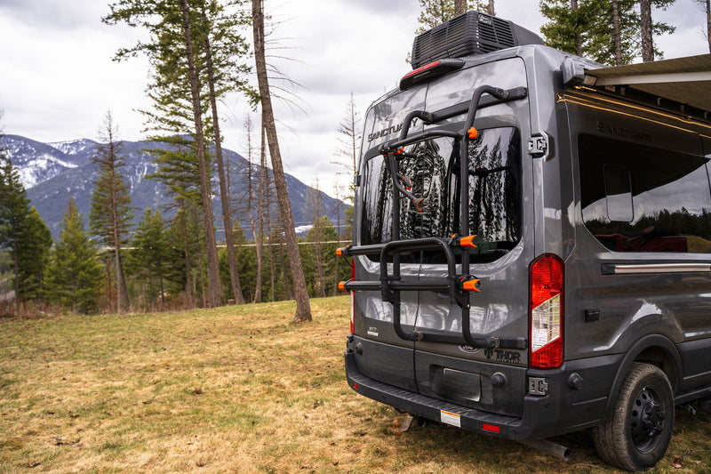  and fruit on a pull-out table for an outdoor picnic experience.|Experience comfort in this RV rental bedroom with fishing-themed quilt & pillows. Enjoy forest views from your camper van.|Modern gray rv rental van — photo 9