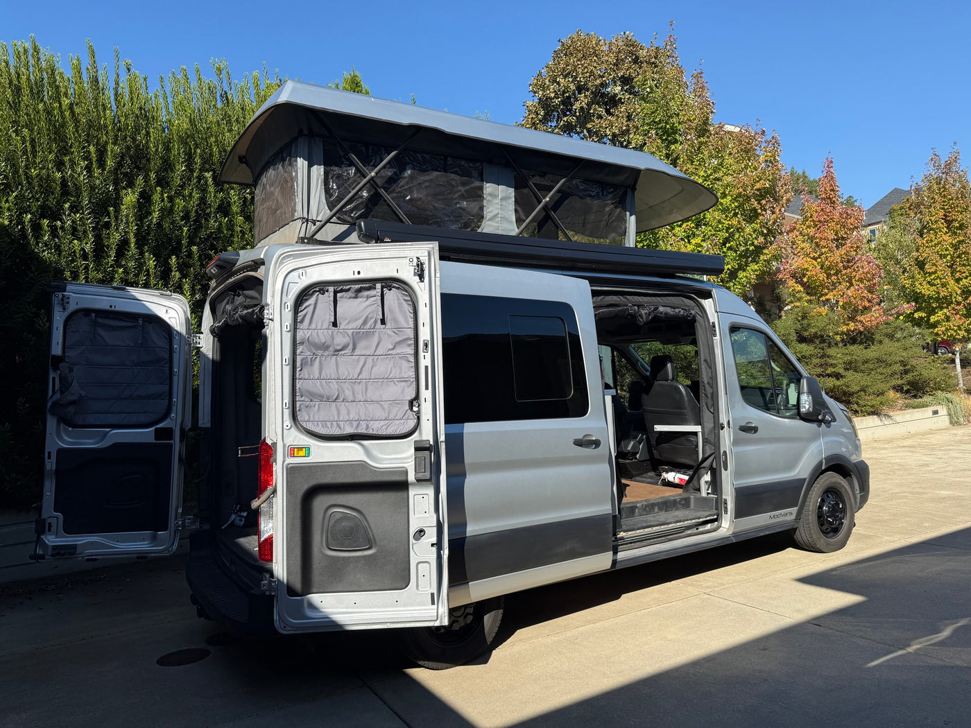 RV rental ready: A grey pop-top Ford Transit camper van with rear and side doors open, showing its adventure setup. — photo 5